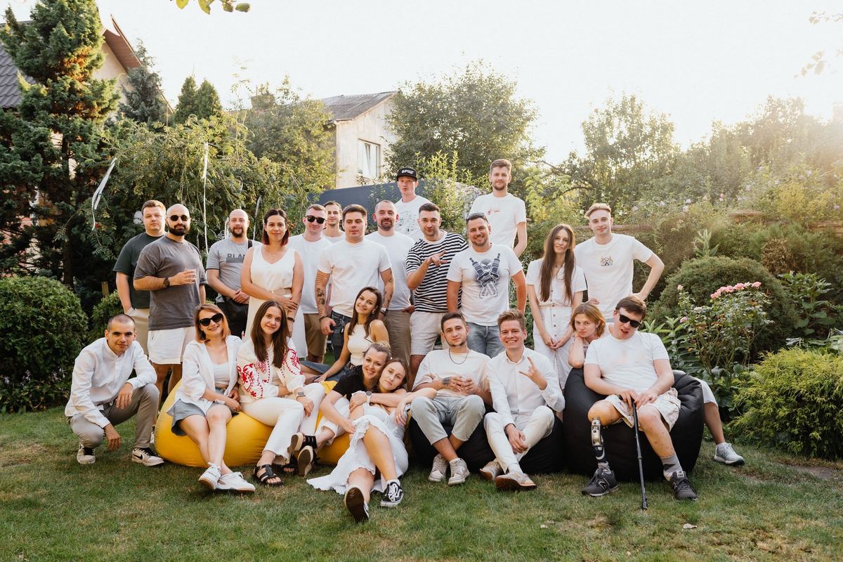 Un grup mare de prieteni zâmbitori adunați pentru o fotografie de grup într-o grădină verde, într-o seară de vară