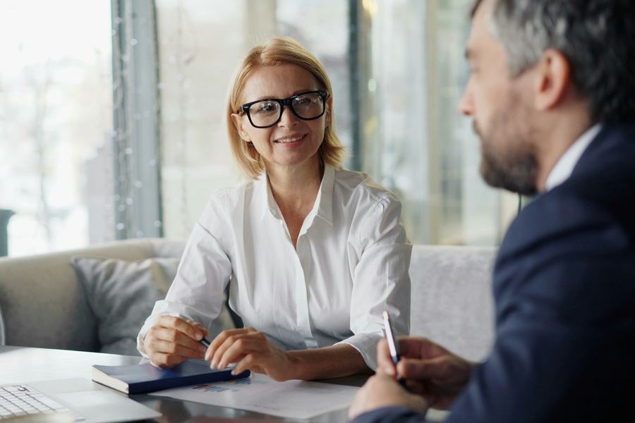 O consultantă zâmbitoare stă de vorbă cu un client la o masă, cu un caiet de notițe în față